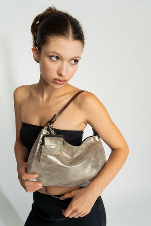 A woman wearing a black sleeveless top and black pants holds an INA KENT metallic handbag while looking to the side.