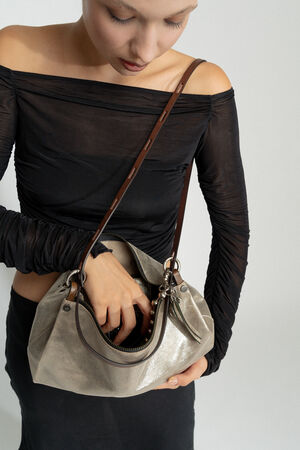 Eine Person in einem schwarzen, schulterfreien Top und Rock blickt in eine beige INA KENT Handtasche mit braunem Riemen.