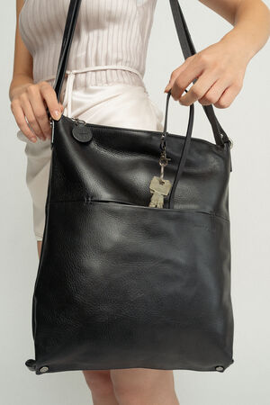 Person holding a large black leather INA KENT tote bag with keys clipped to the front zipper. The person wears a light-colored top and skirt.