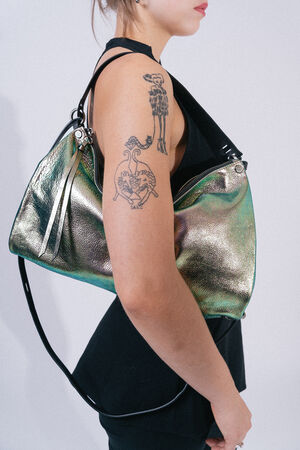 A person with tattoos on their upper arm is wearing a sleeveless black top and carrying a metallic, large shoulder bag from INA KENT.