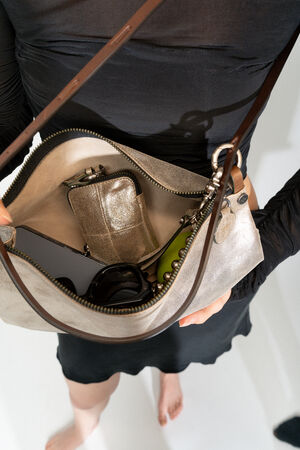 Person holding an open INA KENT handbag containing a phone, a metallic wallet, keys, and other small items, viewed from above.