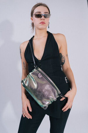 A person wearing sunglasses, a black sleeveless outfit, and an INA KENT metallic crossbody bag poses confidently. The individual's arms reveal various tattoos.