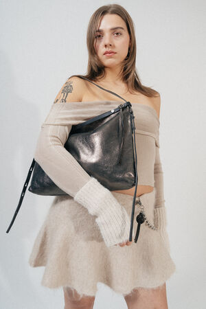 A woman is posing with an INA KENT black leather shoulder bag, wearing a beige off-shoulder top and a beige flared skirt, with long fingerless gloves. She has a tattoo on her shoulder.