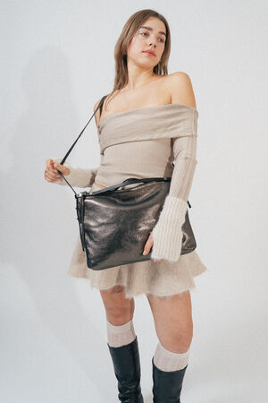 A person stands against a plain background wearing a beige off-shoulder sweater, a matching skirt, knee-high socks, black boots, and holding an INA KENT metallic handbag over one shoulder.