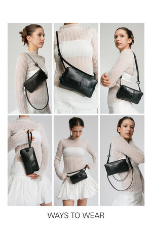 Ein Modell demonstriert die Vielseitigkeit der schwarzen Leder-Umhängetasche INA KENT, elegant kombiniert über einem transparenten gestreiften Oberteil und einem weißen Rock.