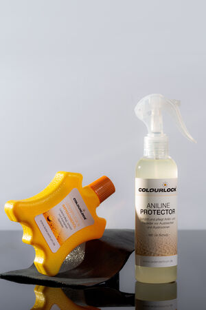 Two leather care products sit on a reflective surface: a yellow sponge shaped like a leather symbol, and a spray bottle labeled "COLOURLOCK Aniline Protector," reminiscent of INA KENT's commitment to quality and style.