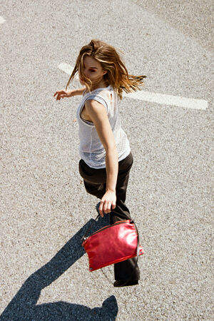 A person strolls down the road, glancing back with a confident air while holding a stylish INA KENT red bag.