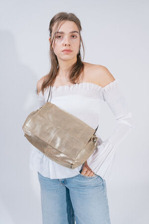 A person wearing a white off-the-shoulder top and blue jeans is holding a large beige INA KENT bag across their body.