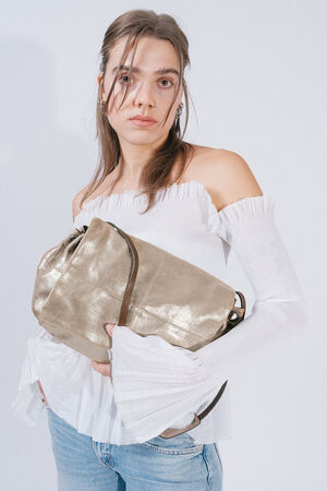 A person with long hair wearing an off-the-shoulder white top and jeans is holding a large metallic INA KENT bag with a handle.