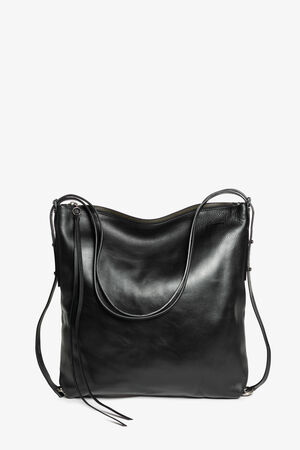 The INA KENT black leather tote bag, featuring long shoulder straps and a chic tassel detail on one side, stands elegantly against a plain white background.