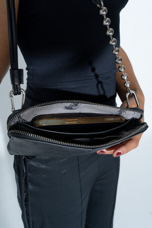 Nahaufnahme einer geöffneten INA KENT Schultertasche IVIET ed.1 in True Black, getragen von einer Person in schwarzer Kleidung. Im Hauptfach ist ein Smartphone sichtbar, die Tasche ist durch einen markanten, metallischen Kugelriemen an der Schulter befestigt.