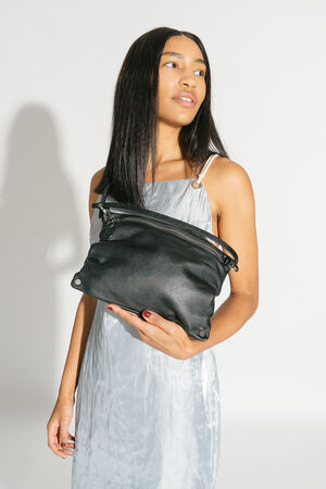 The MOONLIT ed.1 bag in natural black is held in the arms of a model wearing an elegant silver dress. The soft leather and striking design elements make it a statement piece.