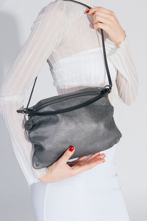 Woman in a white, translucent top and white skirt carries the INA KENT MOONLIT ed.1 bag over her shoulder. The structured, black bag is shown from behind at an oblique angle.