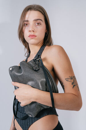Woman with a neutral expression holds the INA KENT bag MOONLIT ed.1 in Honeycomb Black in front of her body. The bag has a striking, textured surface.