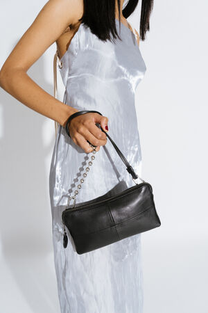 INA KENT IVIET ed.2 natural true black (sideways, held on the wrist): An elegant black bag with a simple design and a silver ball chain as a strap, held by a person in a shiny, silver-colored dress.