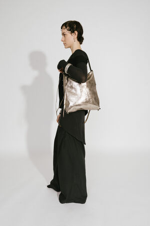 Model mit INA KENT AMPLE ed.1 metallic bright anthra (seitlich, getragen): Die Tasche wird seitlich getragen und präsentiert ihre leicht strukturierte metallic-anthrazitfarbene Oberfläche. Das Model trägt ein modernes, monochromes Outfit, das die Tasche in den Mittelpunkt stellt.