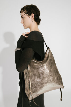 Model with INA KENT AMPLE ed.1 metallic bright anthra (side view): The bag is presented in side view, worn by the model over the shoulder. The focus is on the metallic shine and the generous shape of the bag. The model is wearing a modern, black outfit with stylish accessories.