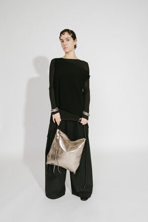 del mit INA KENT AMPLE ed.1 metallic bright anthra (Vorderansicht, stehend): Das Model hält die Tasche in der Hand und steht frontal zur Kamera. Die glänzende metallic-anthrazitfarbene Oberfläche und die praktische Größe der Tasche werden betont. Schwarze, minimalistische Kleidung ergänzt die elegante Ästhetik.