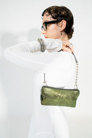 Seitenansicht einer weiblich gelesenen Person, die die INA KENT Tasche IVI ed.3 in crackled guacamole Leder über der Schulter trägt. Die Tasche hat eine silberne Kugelkette und wirkt auffällig durch ihren grünen Metallic-Glanz.