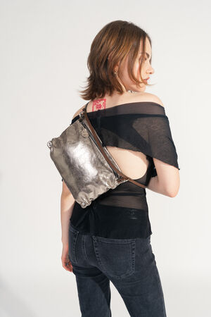 Female read person carries the INA KENT MOONLIT ed.1 bag in metallic bright anthra across the back. The bag looks light and adapts to the shape of the body, the strap runs diagonally.