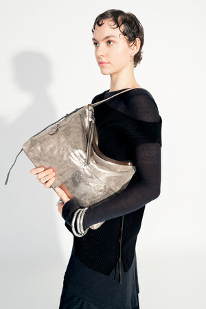 Model with INA KENT ROVE ed.3 metallic bright anthra (in hand, front view): The model holds the bag in front of her with both hands, emphasizing the shiny metallic anthracite surface and the practical size. The bag looks modern and versatile.