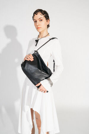 INA KENT DINKUM ed.2 natural true black (frontal, getragen): Eine elegante schwarze Tasche, die frontal von einer Person präsentiert wird. Die Tasche ergänzt den modernen, zurückhaltenden Look des Outfits.