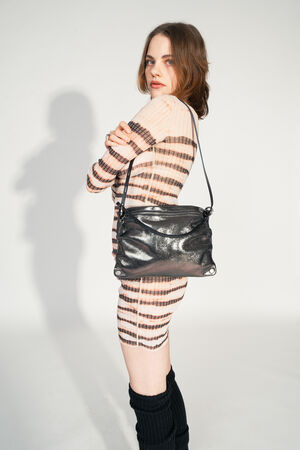 INA KENT MOONLIT ed.1 crackled graphite (worn on the side): A person in a striped, semi-transparent dress wears the MOONLIT ed.1 bag in the color Crackled Graphite sideways over the shoulder. The shiny metallic surface of the bag reflects the light, while the simple strap complements the modern look.