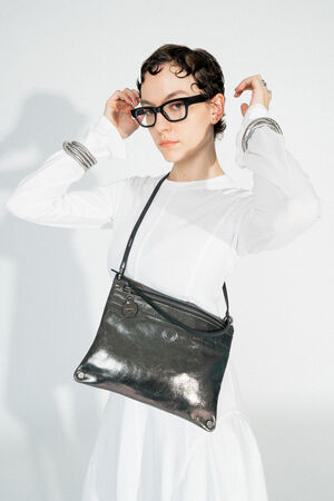INA KENT MOONSTRUCK ed.1 crackled graphite (worn on the side): The bag is worn on the side of the shoulder and stands out with its shiny, graphite-colored surface. The black strap and minimalist design go perfectly with the white dress.