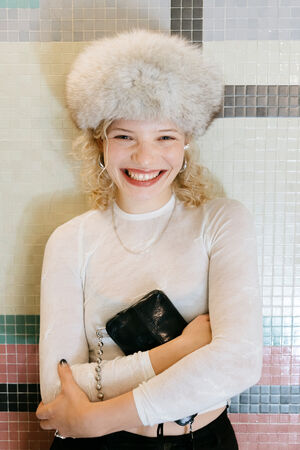 Close-up of Luisa Gaffron in front of a colorful tiled wall. She holds a small black INA KENT bag in her arms and laughs heartily.