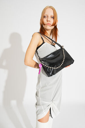 Model trägt die INA KENT Tasche ORNAMENT ed.2 in patent ink black als Schultertasche mit auffälliger Metallkugel-Kette.