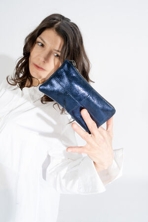 A person in a white shirt holds an INA KENT clutch purse, its shiny blue surface gleaming as they extend it towards the camera.