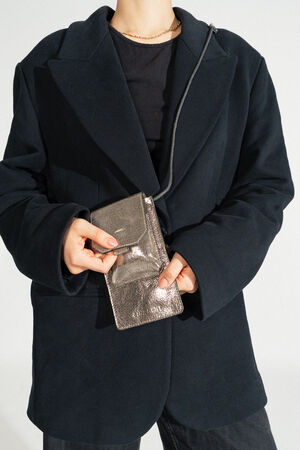 Eine Person im schwarzen Blazer hält elegant eine metallische Handtasche mit Riemen von INA KENT.