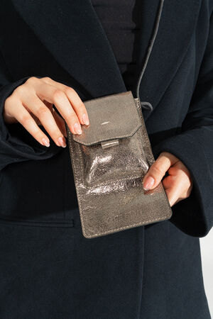 A person in a dark coat holds an INA KENT metallic wallet-style purse with both hands.