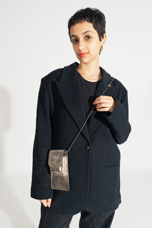 A person with short hair, dressed in a chic black blazer and holding an elegant INA KENT shoulder bag, stands confidently against a plain background.