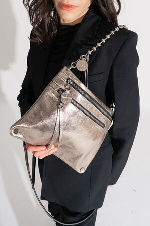Person holding an INA KENT metallic handbag with zippers and a chain strap, wearing a sleek black outfit.