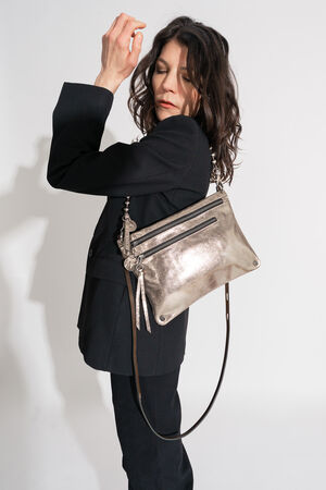 A person in a black suit stylishly holds an INA KENT silver metallic handbag over their shoulder against a plain background.