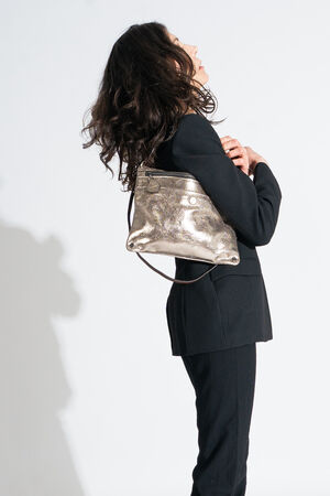 A person in a black suit gazes upward, clutching an INA KENT shiny metallic shoulder bag.