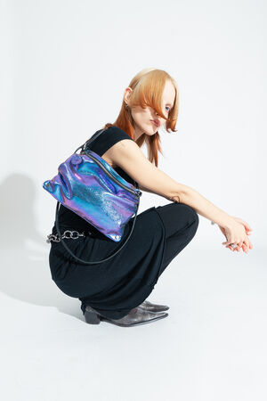 Eine Person in schwarzer Kleidung posiert vor einem weißen Hintergrund mit der zweifarbigen metallic Leder-Crossbody-Tasche MOONLIT ed.1 in Lila-blau 