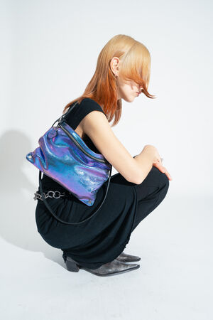 Eine Person in schwarzer Kleidung posiert vor einem weißen Hintergrund mit der zweifarbigen metallic Leder-Crossbody-Tasche MOONLIT ed.1 in Lila-blau 