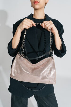 Eine Person in einem schwarzen Blazer hält vor einem schlichten Hintergrund eine schimmernde rosa Handtasche von INA KENT mit einem Perlenriemen.