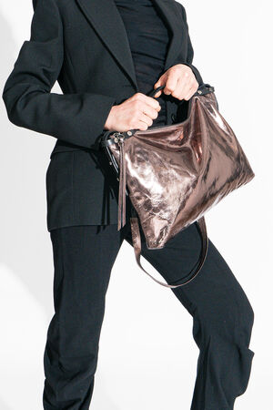 Eine Person im schwarzen Anzug trägt selbstbewusst eine metallische Handtasche mit Schulterriemen von INA KENT und verbindet Eleganz mit Funktionalität.