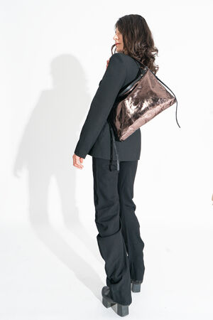 A person in a black outfit poses with an INA KENT reflective brown bag, looking over their shoulder against a white background.