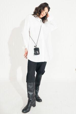 Person wearing an oversized white shirt, black pants, knee-high black boots, and a small INA KENT crossbody bag stands against a plain white background.