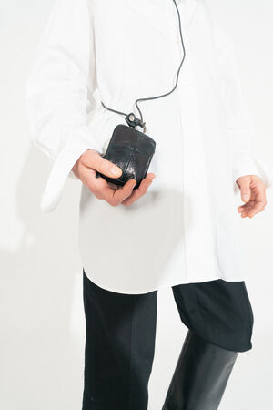 A person in a white shirt and black pants holds a vintage wired computer mouse, embodying a retro yet chic style reminiscent of INA KENT's eclectic fashion aesthetic.