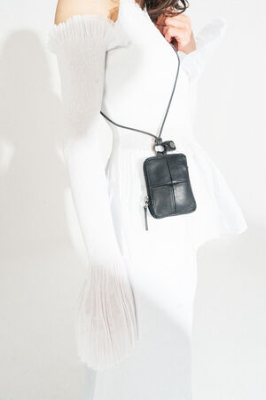 A person in a white off-the-shoulder dress with textured sleeves is elegantly styled, carrying a chic INA KENT small black leather crossbody bag.