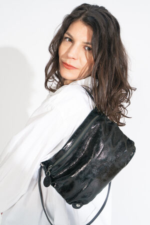 Person with long dark hair wearing a white shirt, confidently carrying an elegant INA KENT shiny black bag over their shoulder, looking at the camera.