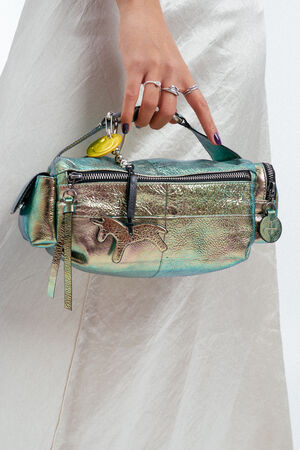 Eine Person mit Ringen hält eine schillernde metallische Handtasche von INA KENT mit einem hundeförmigen Detail und Schlüsselanhängern vor einem hellen Rock.