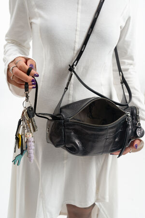 Eine Person im weißen Kleid hält in der einen Hand einen Schlüsselbund mit Schlüsselanhängern und in der anderen eine offene schwarze INA KENT-Umhängetasche aus Leder.