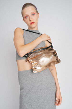 Person with short hair holding an INA KENT metallic handbag, wearing a sleeveless gray crop top and skirt against a plain background.