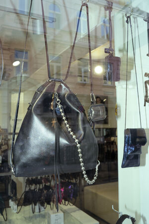 An INA KENT black leather shoulder bag with a chain strap is displayed in a store window alongside several smaller bags and accessories.
